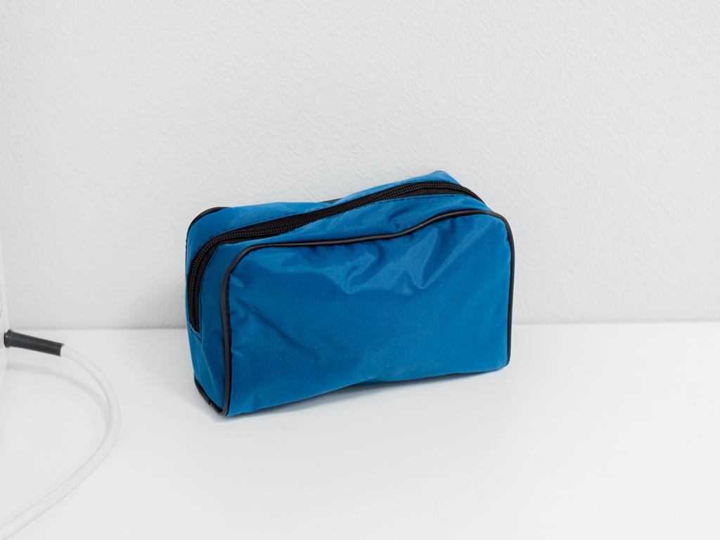 Blue cloth medical bag, cosmetic bag with black zipper stands on white table. First aid kit in light interior