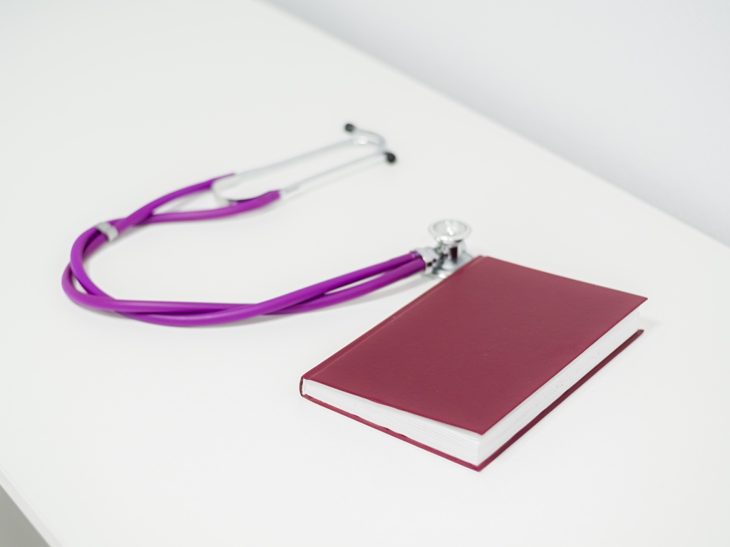 Purple stethoscope and red medical notebook, journal on white table in doctor's cabinet. Close-up.
