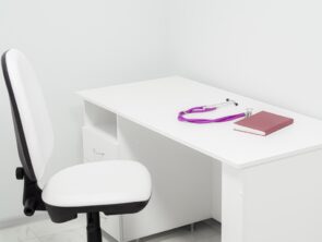 Chair and white table with purple stethoscope and red medical journal in doctor's office. Notebook